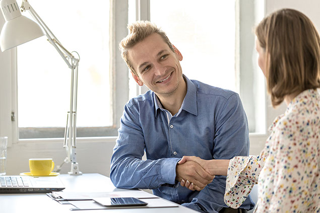 Image of 2 people sitting at desk shaking hands.