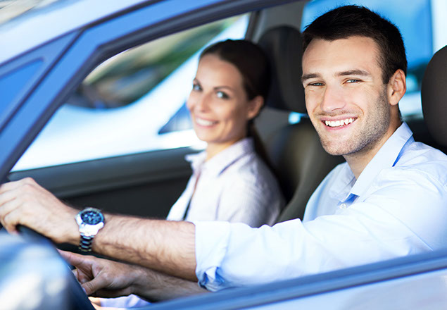 Image of man driving, smiling with a passenger who is also smiling.