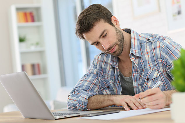 Image of man sitting at the table writing with pen and paper.