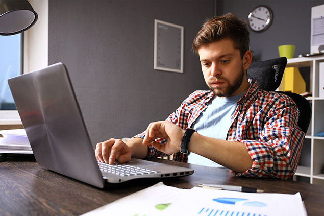 Image of man on laptop checking time on watch.