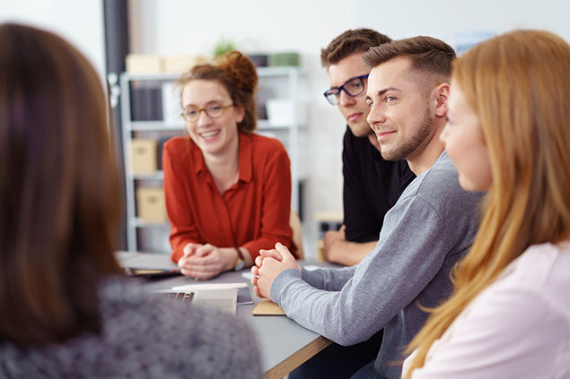 Image of young empolyees in a meeting listening with a smile to a fellow empolyee.