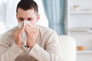 Image of man blowing nose with tissue.