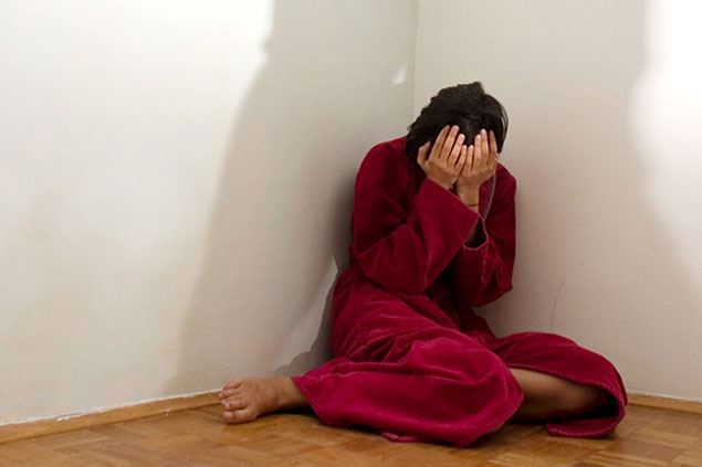 Image of women wearing a robe sitting in the corner with face in hands.