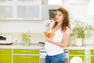 Image of pregnant women eating a bowl of fruit and veggies.
