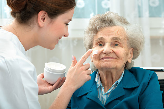 Image of a caregiver placing cream on a mature women's face.