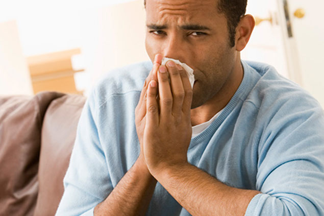 Image of man blowing nose with a tissue.