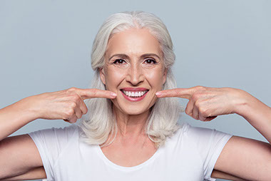 Image of older women smiling and pointing to her mouth.