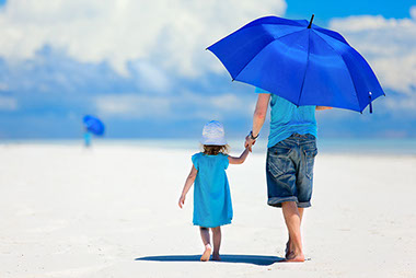 Image of father and child walking on the beach with a big blue umbrella.