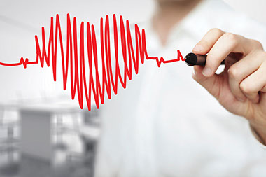 Close up image of a doctor's hand drawing a heart with heart beats.