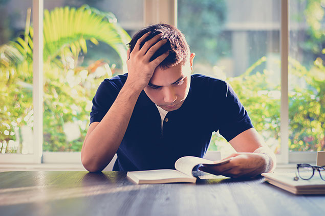 Image of stressed college student reading a text book.