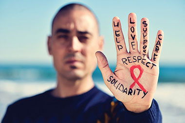 Image of man's hold with the AIDS ribbon and words on fingers, that inlcude 'help', 'love', 'support', 'care.'