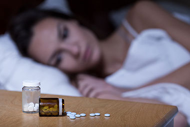 Image of women trying to sleep with pills on her nightstand.