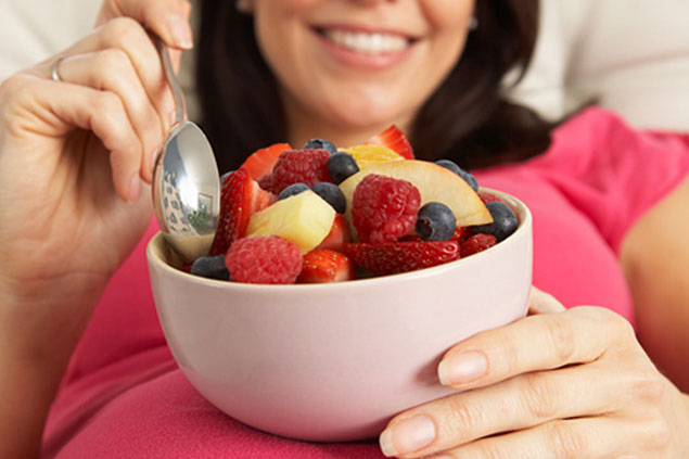 Image of bowl of fruit resting on womens pregnant belly.