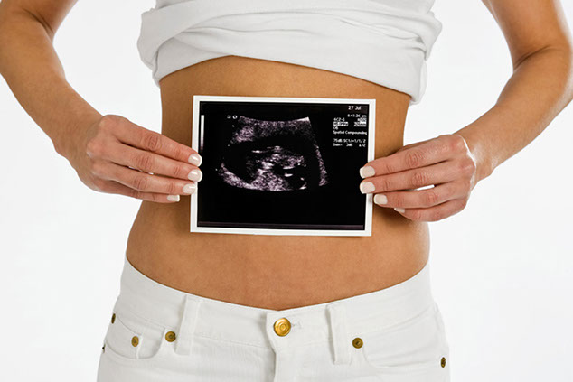 Image of women holding ultrasound photo on bare stomach.
