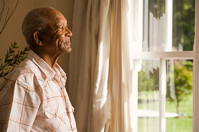 Image of elderly man looking outside his window.