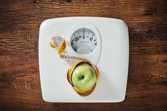 Green apple wrapped in a tape measure on a white scale.