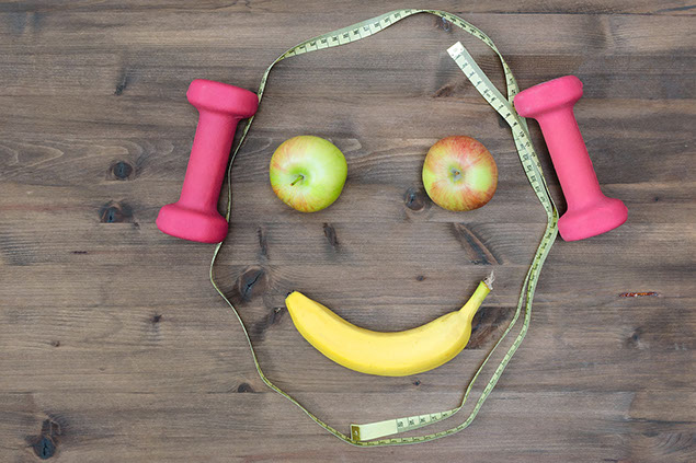 Apples, measuring tape, dumbbells and banana assembled into a smiling face.