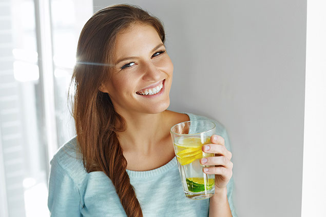 Happy woman drinking water with fresh lemon, lime, and mint.