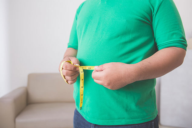Overweight man measuring his belly at home.