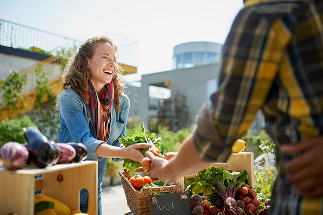 Woman tending stall at a farmers market and selling fresh vegetables.