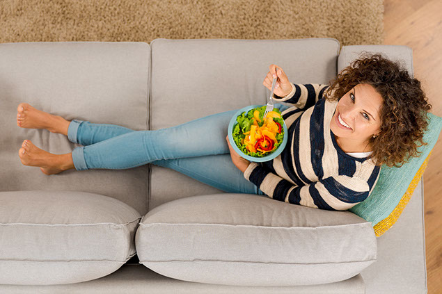Top view of woman on the sofa eating a healthy salad.
