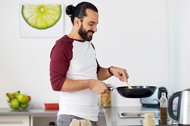 Man with frying pan cooking food at home.
