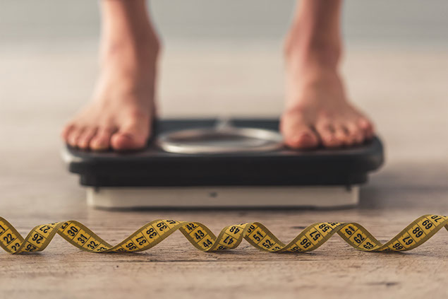 Person standing on scale, with tape measure in the foreground.