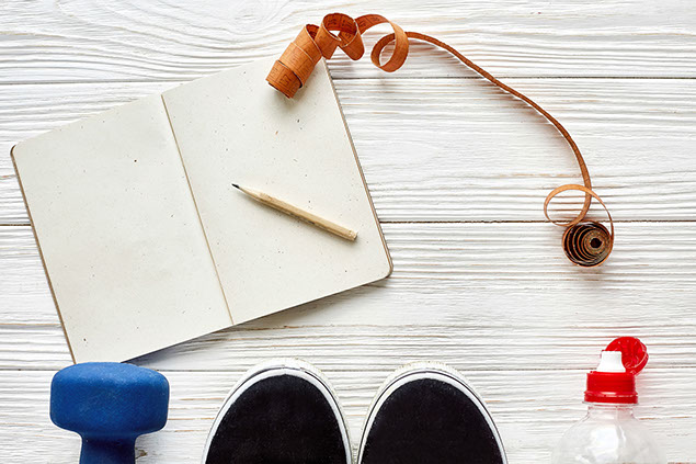 Fitness concept with notebook pencil for sport goals and resolutions, dumbbells and sneakers and water bottle.
