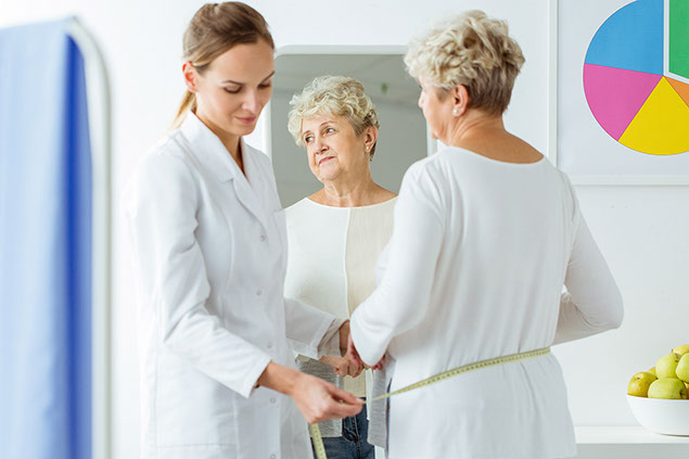 Reflection of patient's face in the mirror and dietician measuring her body circuit.