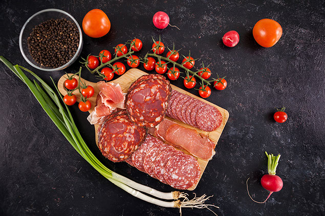 Deli meat on cutting board with fresh tomatoes and green onions.