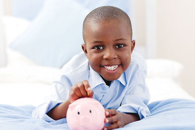 Image of young boy putting coins into a piggy bank.