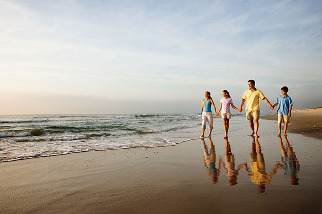 Image of family holding hands while walking along the beach.