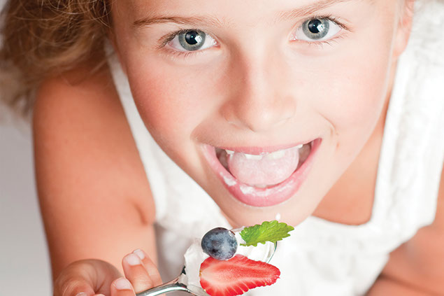 Image of child eating yogurt with strawberries and blue berries.