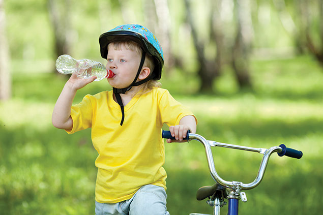 Image of boy drinking water standing next to his bike.
