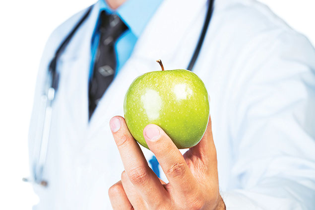 Close-up image of doctor's hand holding a green apple.