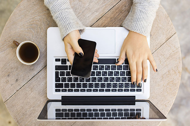 Close up image of laptop with hands and phone.