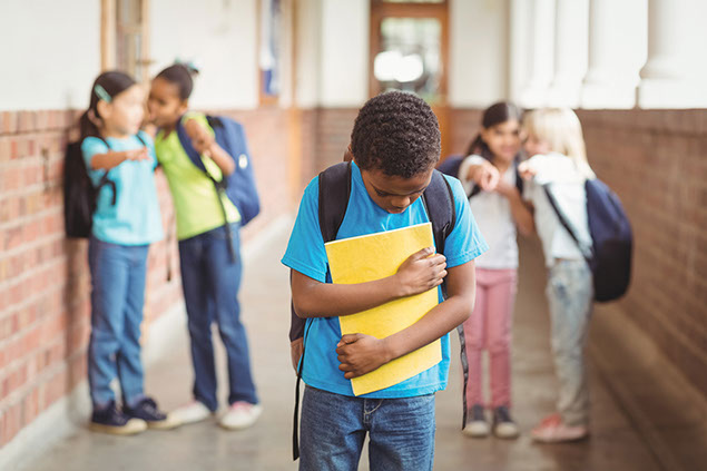 Image of kids wispering and pointing towards a classmate whose head is down.