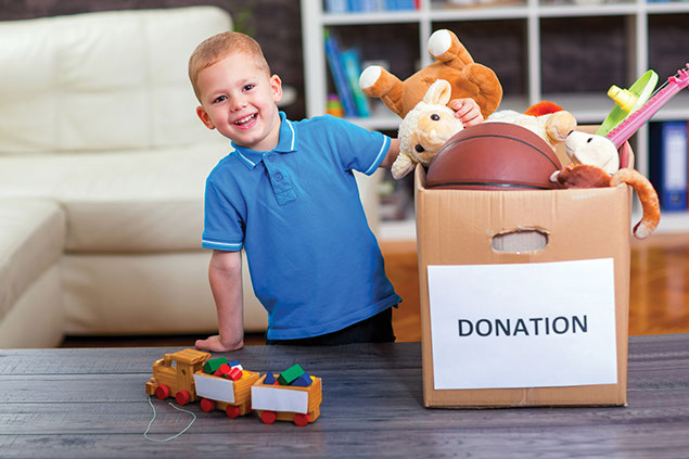Image of happy child placing toys in donation box.