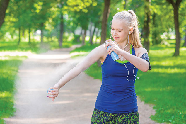 Image of female spraying insect repellent on arm.