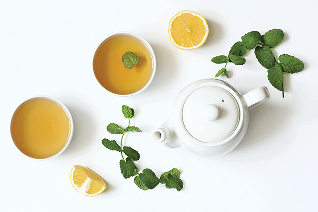 A tea pot with two cups of tea and lemons.