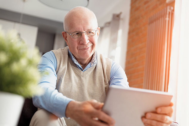 Older man on reading on a tablet.