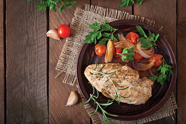 Plate with cooked chicken breast with a side of cooked tomatos and onion.
