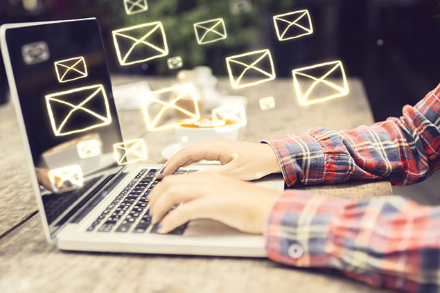 Hands typing on keyboard of laptop with mail concept icons floating.