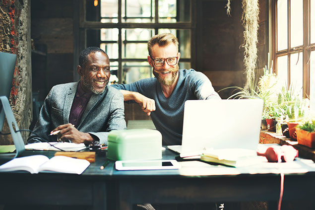 Two coworkers sitting at the table looking at the computer screen.