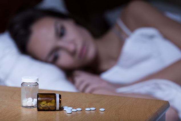 Image of women trying to sleep with pills on her night stand.
