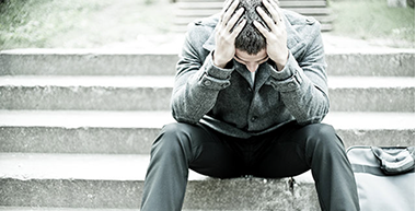 Image of man sitting on stairs with head down in his hands.
