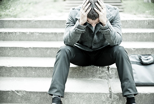 Image of man sitting on stairs with head down in his hands.