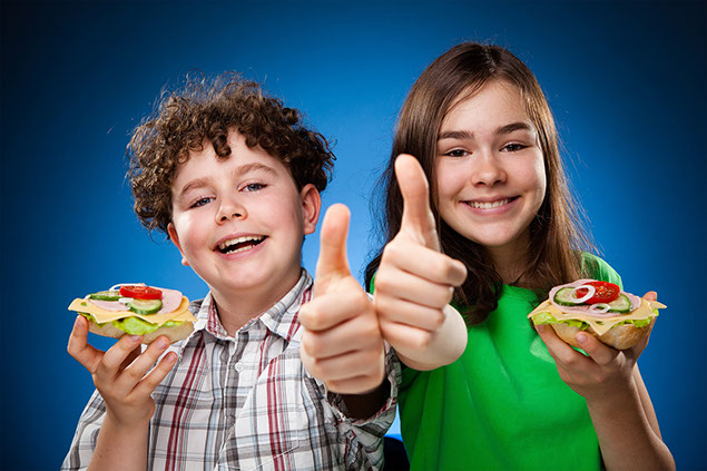 Image of 2 kids holding a healthy snack in one hand and a thumbs up with the other hand.