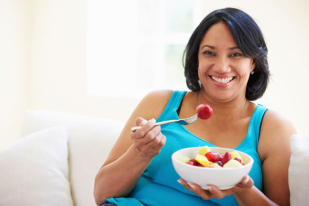 Image of women smiling while eating a bowl of fruit.