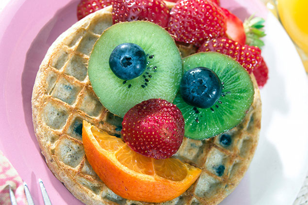 Image of a face made out of fruit on a waffle.